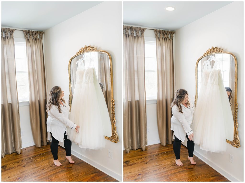Bride touching wedding gown hanging on gold mirror at Pine Knoll Farms wedding venue