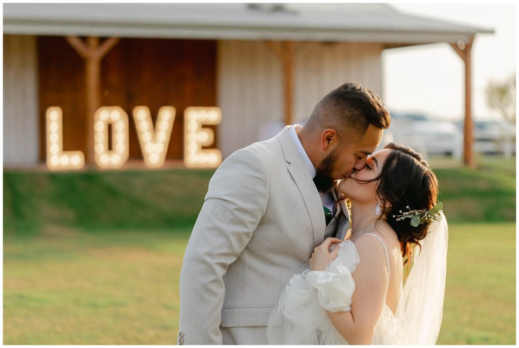 Bride and groom kissing with love marquee in background