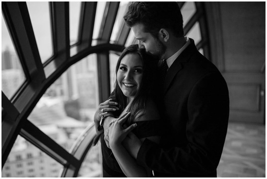 BW Guy hugging girl from behind in front of large window