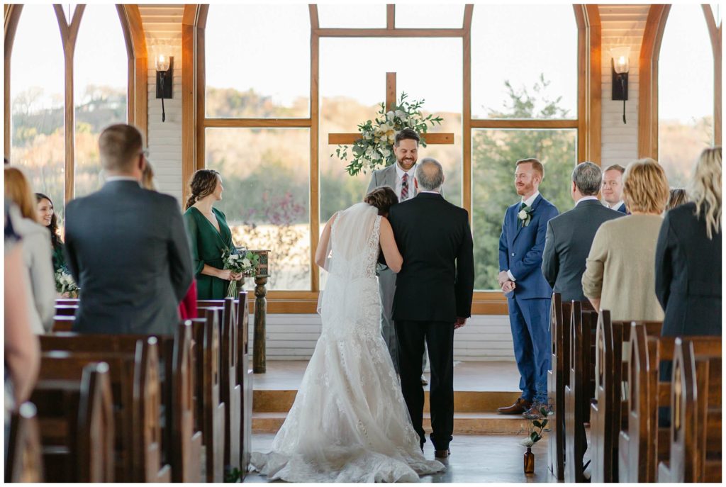 bride leaning head on fathers shoulder at alter