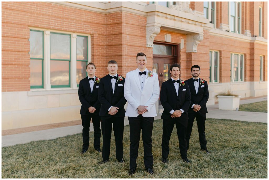 Groom in white standing with groomsmen in black