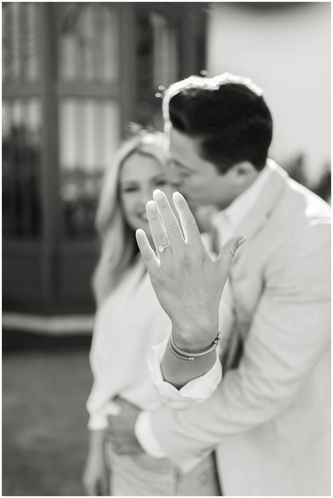 BW girl holding up engagement ring while fiancé kisses her