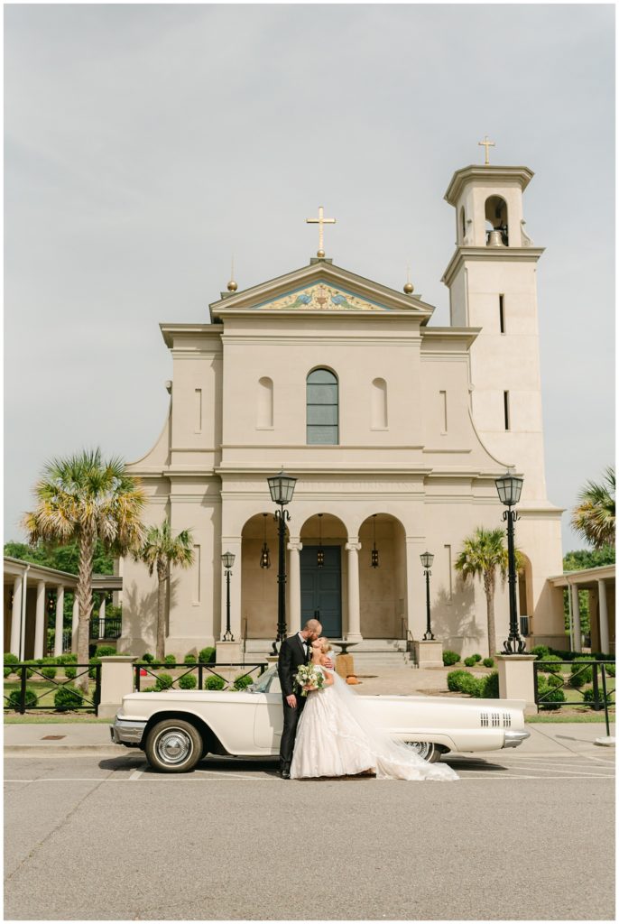 bride and groom kissing in front of chapel and vintage car South Carolina Catholic wedding