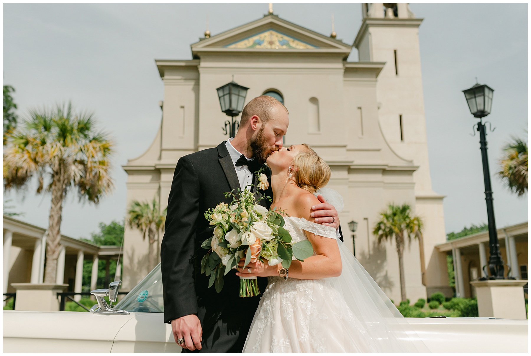 bride and groom kissing in front of chapel and vintage car South Carolina Catholic wedding