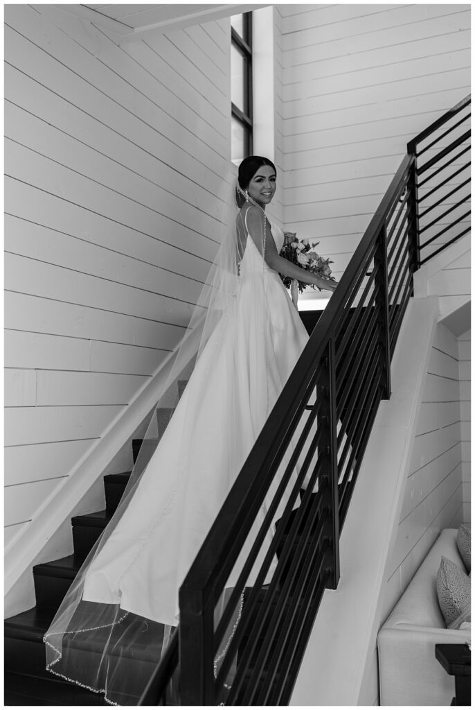 BW bride standing on staircase with gown trailing down steps